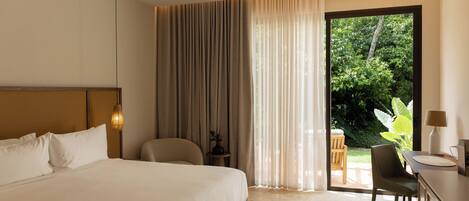 Habitación de hotel con una cama grande, un escritorio, una silla, una mesita y vistas al exterior con zonas verdes.