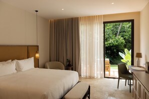 Een hotelkamer met een groot bed, een bureau, een stoel, een kleine tafel en uitzicht op groen buiten.