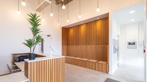 A reception area with a wooden reception desk, a potted plant, a desk lamp, and a seating area with wooden slats. - Station Noir | Stylish 1-Bed in Central MK (Milton Keynes)