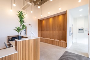 A reception area with a wooden reception desk, a potted plant, a desk lamp, and a seating area with wooden slats.