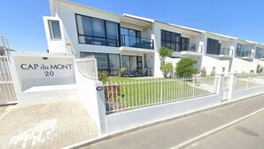 Un immeuble résidentiel moderne à plusieurs étages, doté d’une façade blanche, de grandes fenêtres et d’une entrée sécurisée par un portail.