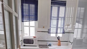 Pieni, käytännöllinen keittiö, jossa on valkoiset kaapit, mikroaaltouuni, pesuallas ja pyykinpesukone.