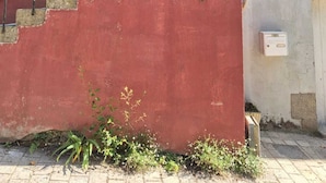 Un bâtiment avec un mur rouge, une porte noire et une fenêtre avec des volets blancs.