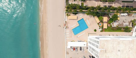 Vista aerea di un hotel fronte spiaggia con piscina, area spiaggia e parcheggio.