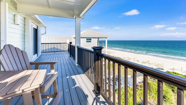 A wooden deck with chairs, a covered area, and a view of the beach and ocean.