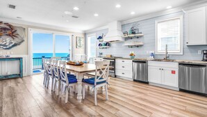 A kitchen with a view to the ocean, wooden flooring, and white cabinetry.