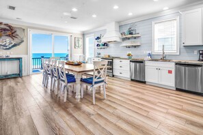 A kitchen with a view to the ocean, wooden flooring, and white cabinetry.