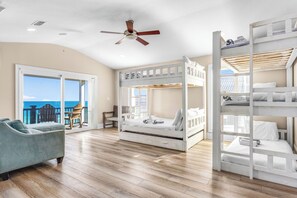 A room with a bunk bed, a sofa, a ceiling fan, and a view of the ocean. - Headed West - Private Pool, Beach Front, Pet Friendly, Beach Gear Included! (St. George Island)