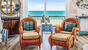 A room with wicker chairs, a ceiling fan, a large mirror, and a view of the ocean.