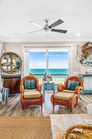 A room with wicker chairs, a ceiling fan, a large mirror, and a view of the ocean.
