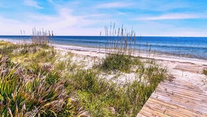 A beach with a wooden boardwalk, sandy dunes, and tall grasses.