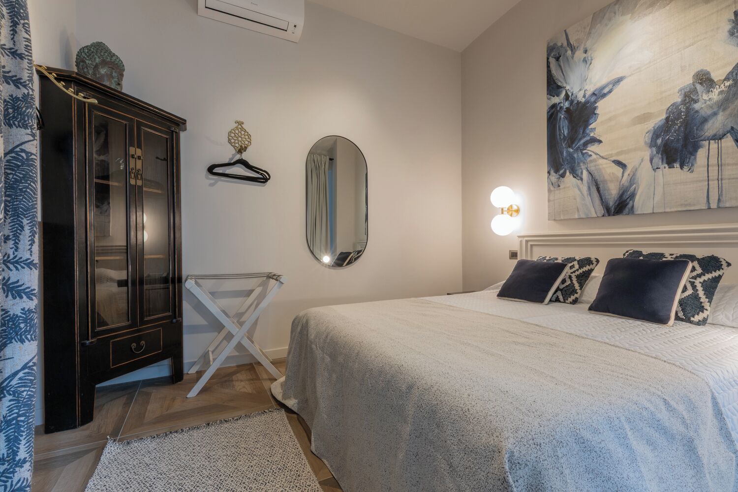 A bedroom with a bed, a wardrobe, a mirror, and a painting on the wall.