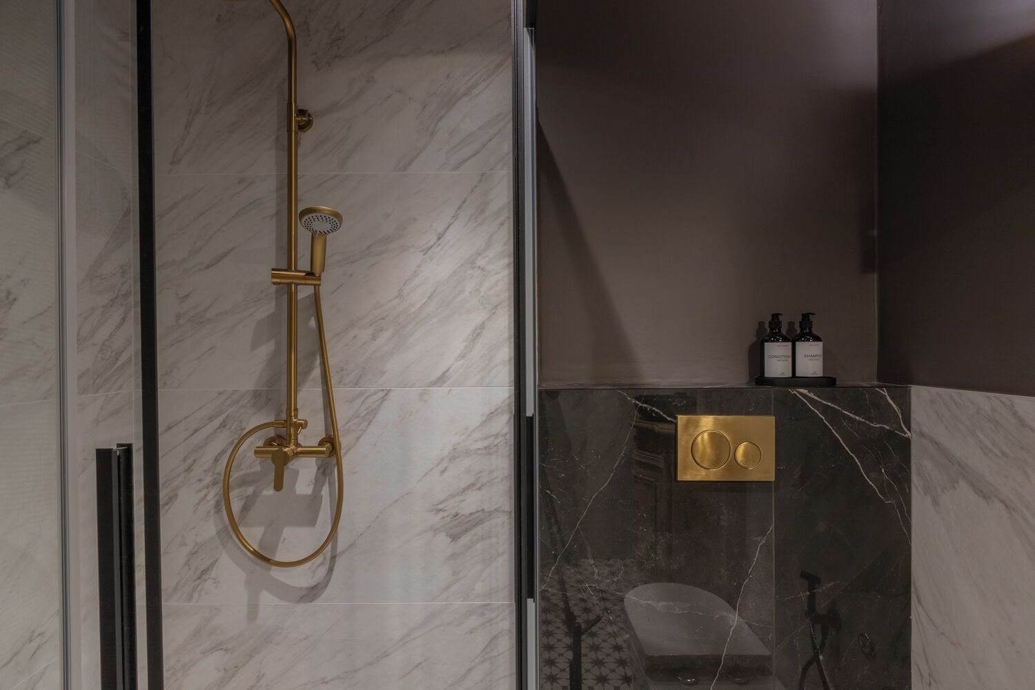 A modern bathroom with a glass-enclosed shower, marble walls, and a vanity with toiletries.