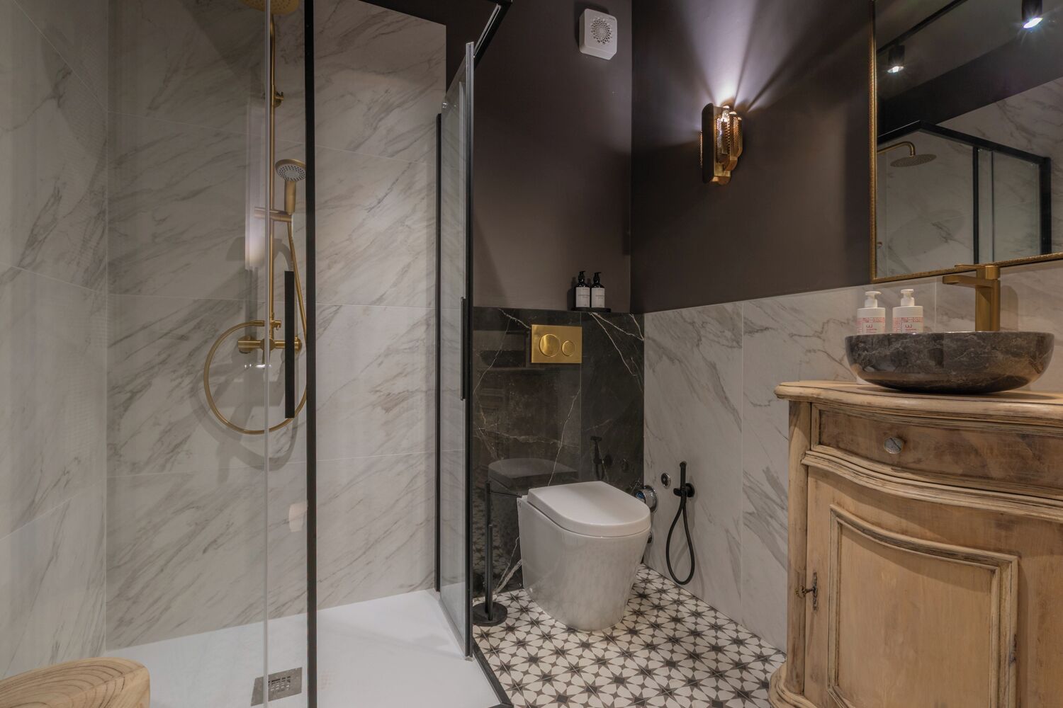 Un baño moderno con cabina de ducha de vidrio, suelo de mármol, tocador de madera y un espejo grande.