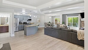 A spacious living area with a large gray sofa, a kitchen with modern appliances, and a dining area with a table and chairs.
