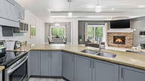 A modern kitchen with granite countertops, grey cabinets, a built-in oven, and a stone fireplace.