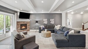 A modern living room with a stone fireplace, grey sofas, a coffee table, and a flat-screen TV mounted on the wall.