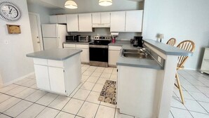 Cocina compacta con armarios blancos, una isla central y un comedor con sillas de madera.