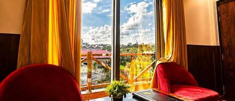 A room with a large window, two red chairs, a wooden table, and a view of a park and buildings.