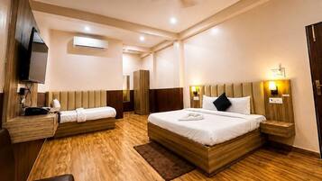 Habitación de hotel con una cama grande, una cama más pequeña, un escritorio, una silla, un televisor y un ventilador de techo.