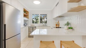 A modern kitchen with white cabinetry, a stainless steel refrigerator, a built-in oven, and a large island with stools. - Tugun Bliss - Absolute Beachfront in Tugun - Min. 3 Night Stays - Linen Provided (Tugun)