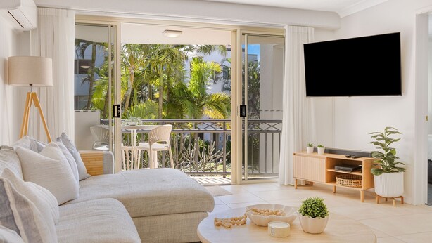 A modern living room with a sofa, a flat-screen TV, and a balcony with a table and chairs. - Tugun Bliss - Absolute Beachfront in Tugun - Min. 3 Night Stays - Linen Provided (Tugun)