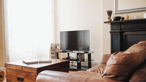 A living room with a leather sofa, a wooden coffee table, a flat-screen TV on a black stand, and a fireplace mantel with decorative items. - Traditional Central 2-Bed Apartment (Edinburgh)