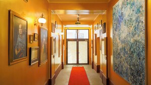A hotel hallway with framed portraits, a red carpet, and a large abstract painting on the right wall. - Sunny Boutique Studio, 57 m², Art Nouveau hotel, ideal for extended stays (Wien)
