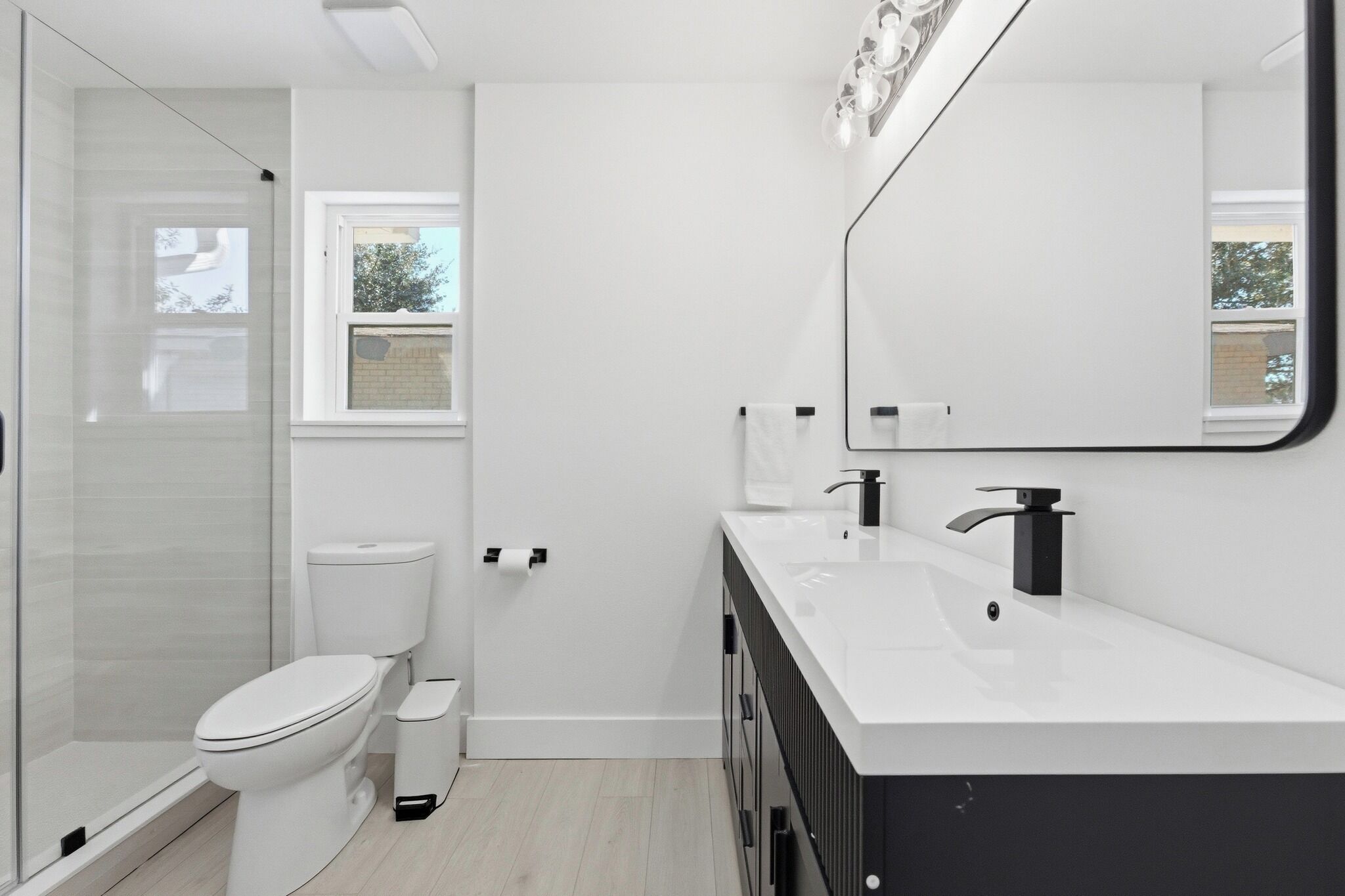 A modern bathroom with a glass shower enclosure, a white toilet, and a black sink with a large mirror above it.