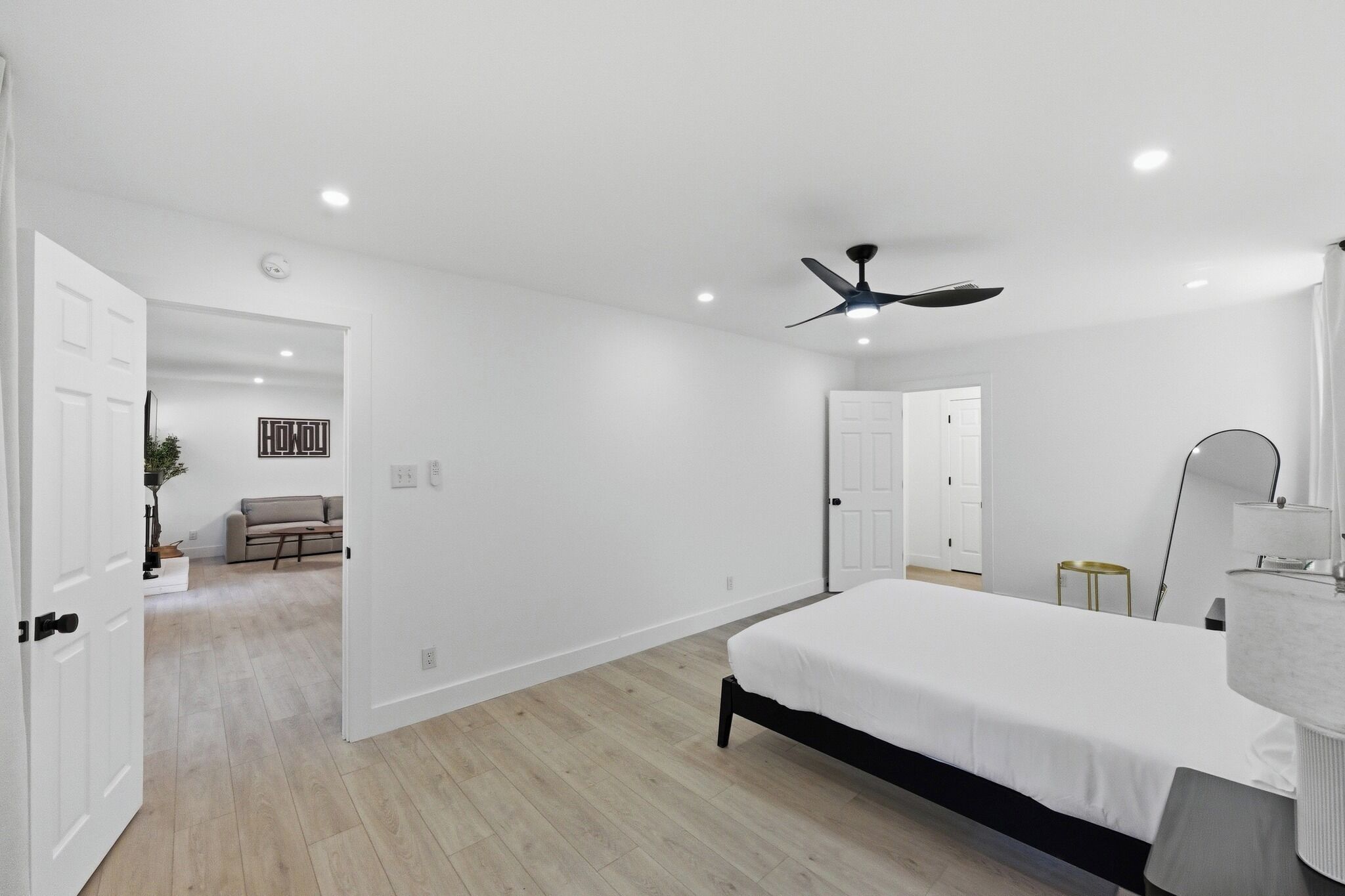 Een moderne slaapkamer met een bed, plafondventilator en een badkamer met spiegel.