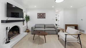 A modern living room with a fireplace, a grey sofa, a coffee table, and a TV mounted above the fireplace. - Austin Escape: Stylish 3BR/4 Beds + Private Pool (Austin)