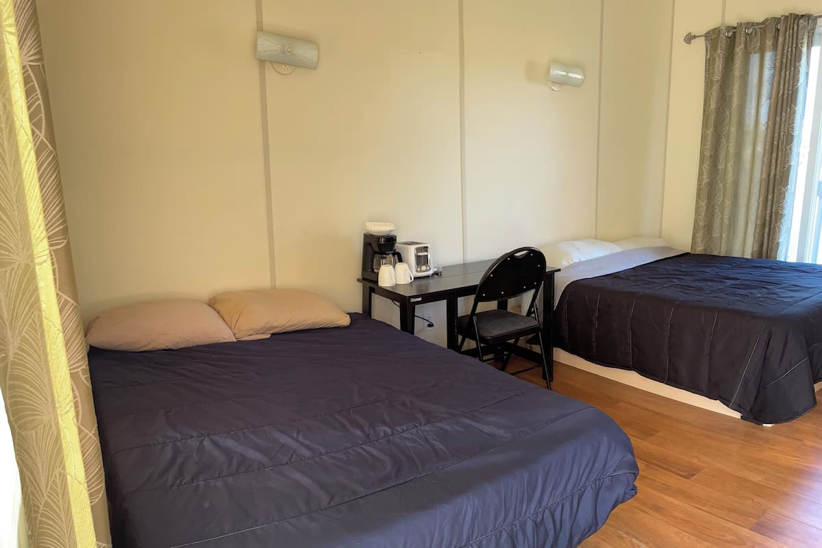 A room with two beds, a desk with a coffee maker, a chair, and a window with curtains.