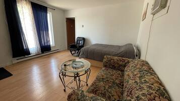 Quarto com sofá floral, mesa de centro de vidro, poltrona de couro, cama e ventilador de teto.