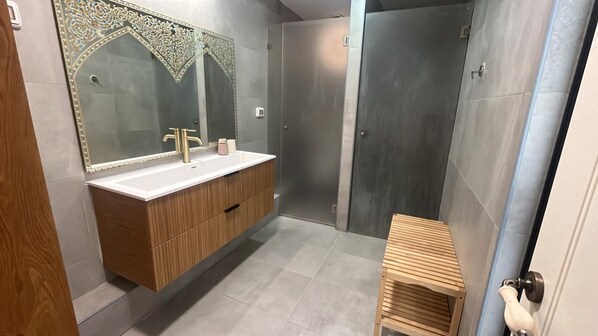Un baño moderno con tocador de madera, un espejo grande y una zona de ducha.