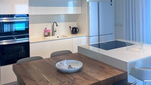 Une cuisine moderne dotée d’appareils électroménagers intégrés, d’une table à manger en bois et de meubles de rangement blancs.