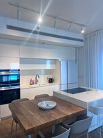 Cozinha moderna com eletrodomésticos embutidos, mesa de jantar de madeira e armários brancos.