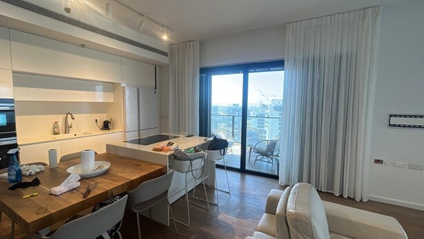 Eine moderne Küche mit Holzarbeitsplatte, weißen Schränken und einem Essbereich mit Holztisch und weißen Stühlen. Ein großes Fenster bietet Blick auf die Stadt.