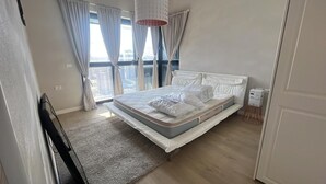 Une chambre avec un grand lit, une vue sur la ville par la fenêtre et un panorama urbain visible à l’extérieur.