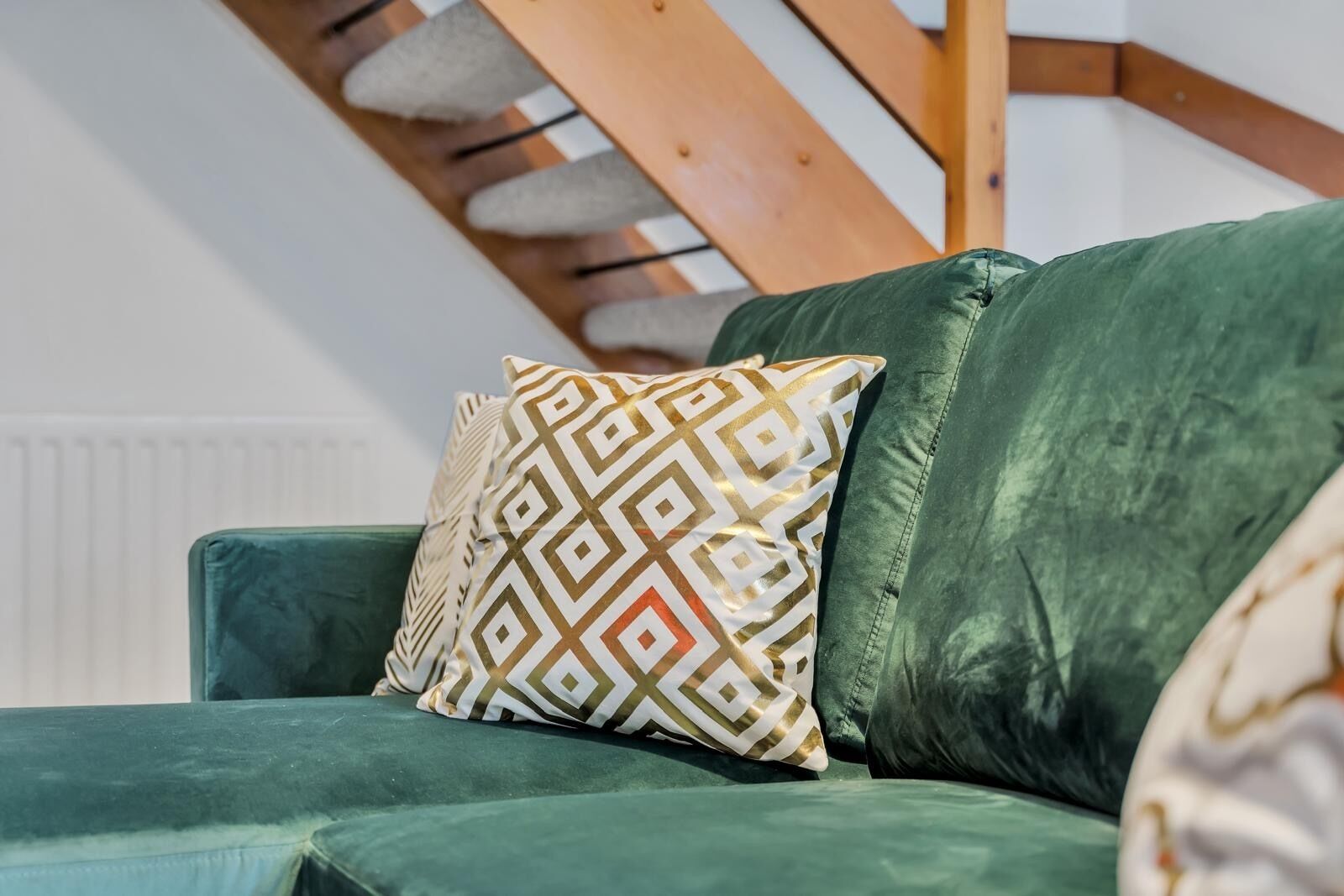 En grön soffa med en mönstrad kudde och en vit radiator i bakgrunden.