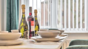 Una mesa de comedor con platos y botellas de vino, frente a una ventana con persianas.