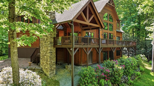 A multi-story wooden cabin with a stone foundation, wooden balconies, and a stone pathway leading to the entrance.