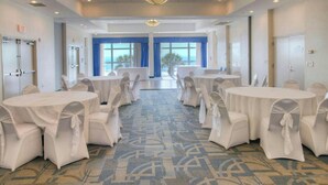 A conference room with round tables and chairs, large windows with blue curtains, and a patterned carpet.