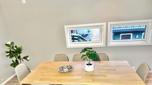 A dining area with a wooden table, six chairs, two potted plants, and framed pictures on the wall.