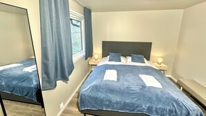 A bedroom with a bed, two bedside tables, a mirror, and a window with curtains.