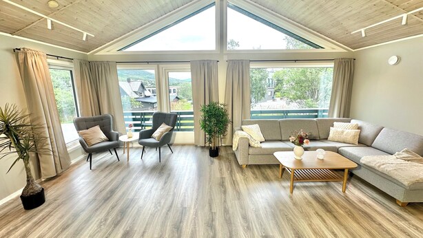 A spacious living room with a high ceiling, large windows, and a view of a balcony.