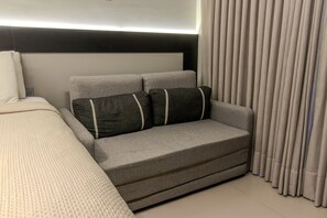 A modern bedroom with a sofa, a bed, and a headboard. - Beach Haus  (João Pessoa)