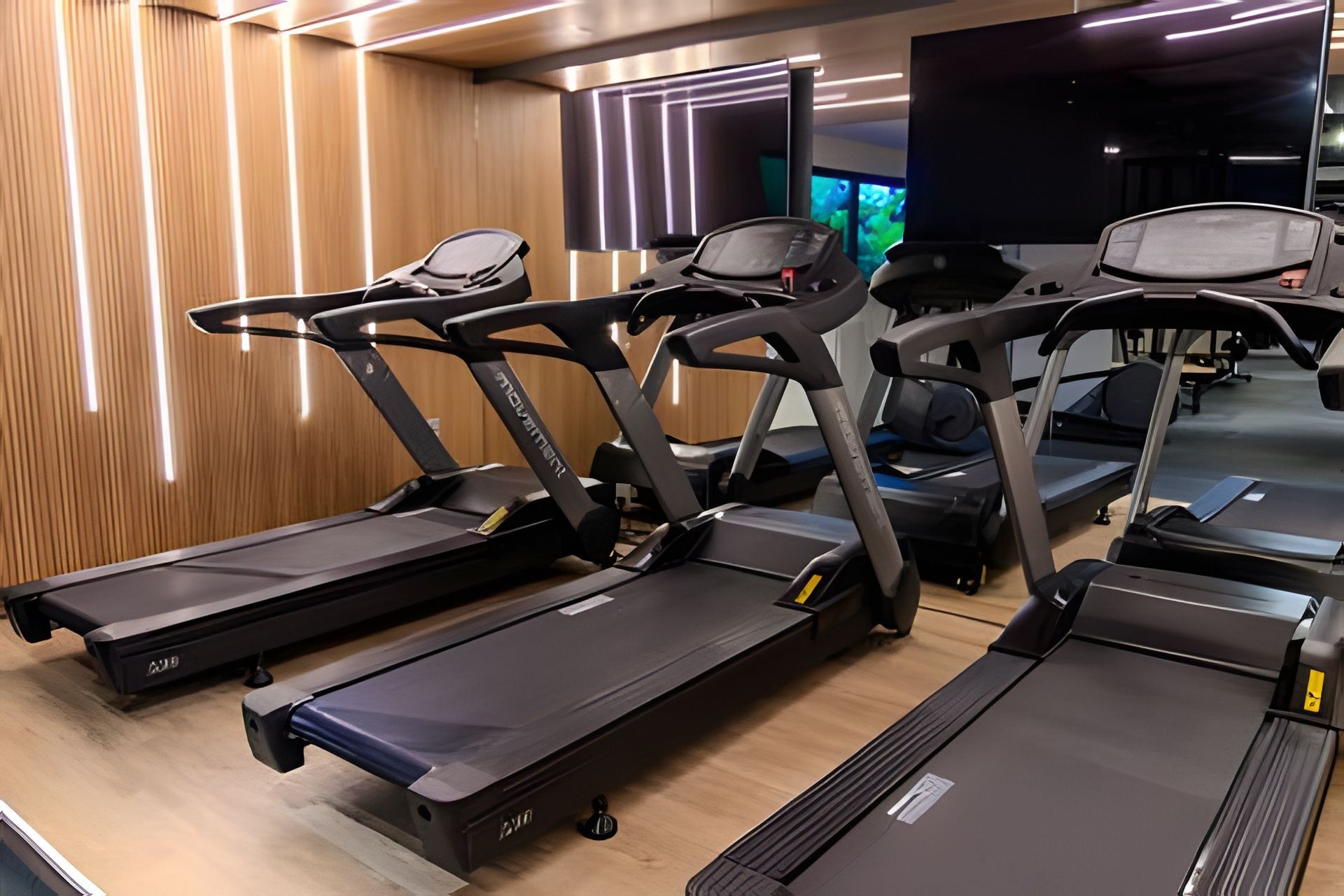 Three treadmill machines in a gym with wooden panel walls and a large screen in the background.
