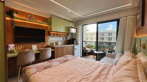 Quarto de hotel com cama, escrivaninha, TV, cozinha compacta e varanda com vista.