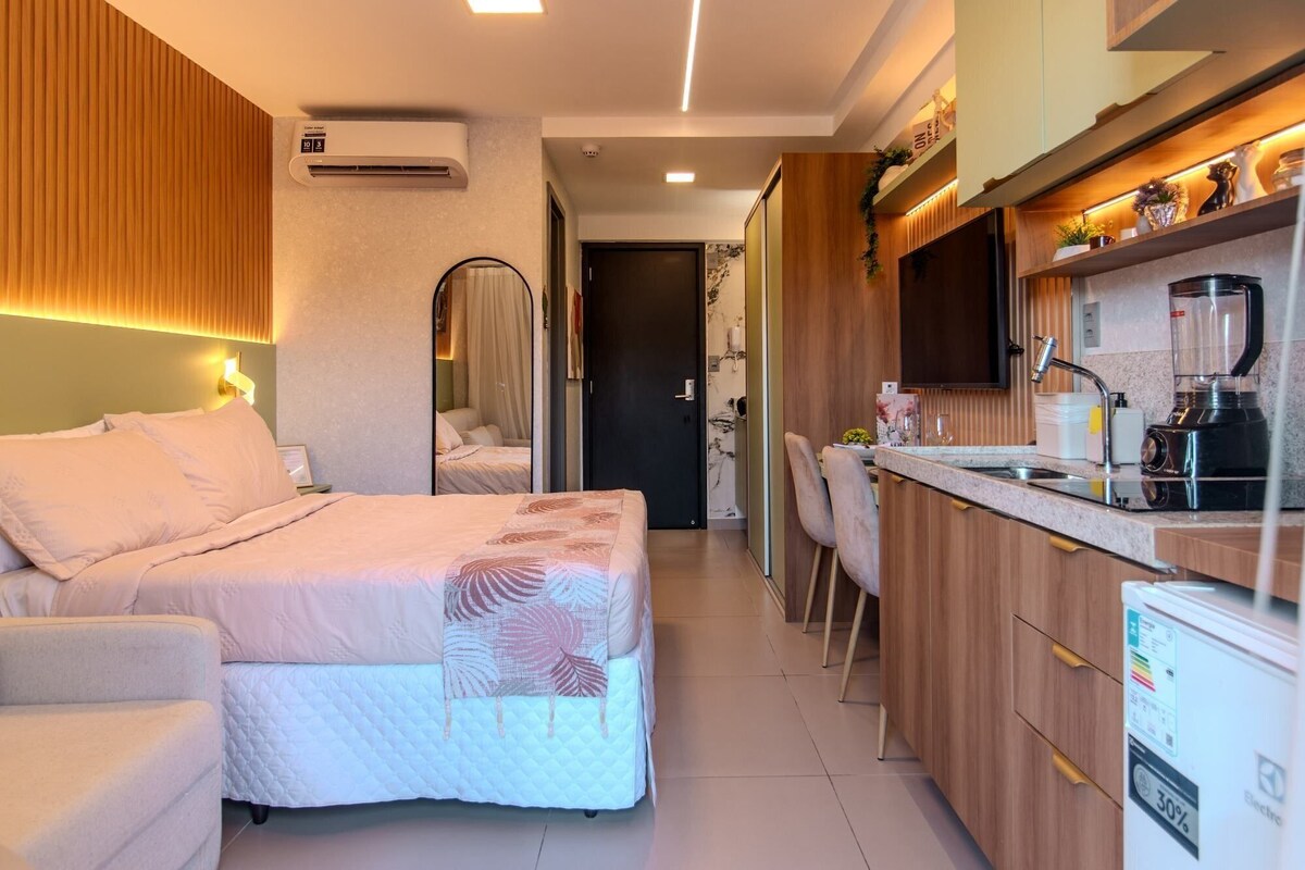 A hotel room with a bed, bedside table, and a kitchenette with a refrigerator, sink, and stove.