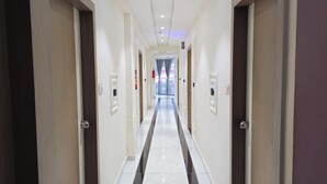 A long, narrow hallway with doors on either side, leading to a bright room at the end. - Hotel Urban View (Ahmedabad)